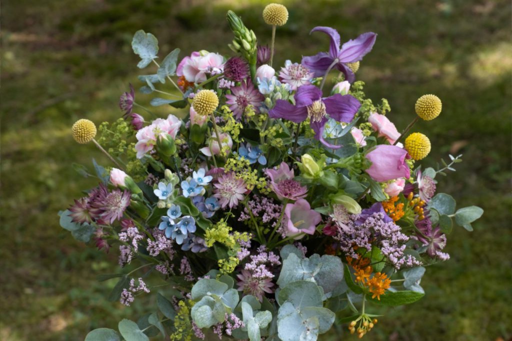 Locker gebundener Sommerstrauß in Rosa, Lila und Blau mit Clematis, Eukalyptus und verschiedenen Wiesenblumen vom Blumenhaus Sander.