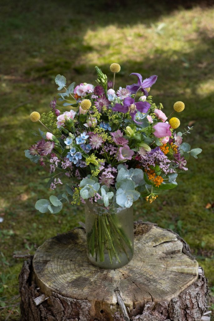 Locker gebundener Sommerstrauß in Rosa, Lila und Blau mit Clematis, Eukalyptus und verschiedenen Wiesenblumen vom Blumenhaus Sander.
