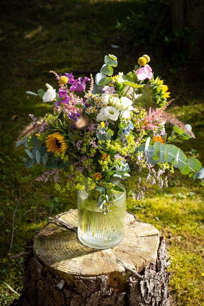 Sommerlicher Blumenstrauß mit Sonnenblumen, weißen Blüten, Kamille, Eukalyptus und Gräsern vom Blumenhaus Sander.